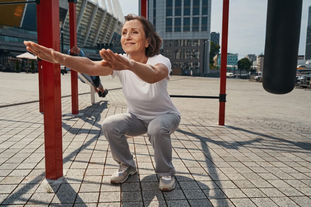 Image of a woman exercising outdoors using good form and technique to prevent knee pain while squatting.
