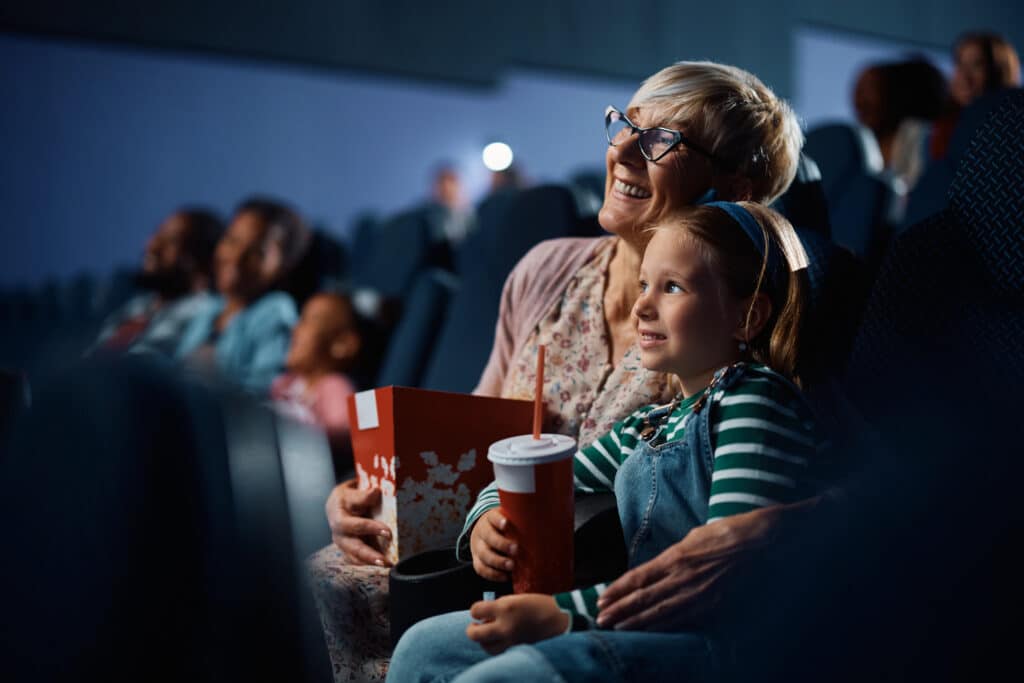 A senior woman and her granddaughter watch a movie in a theater together