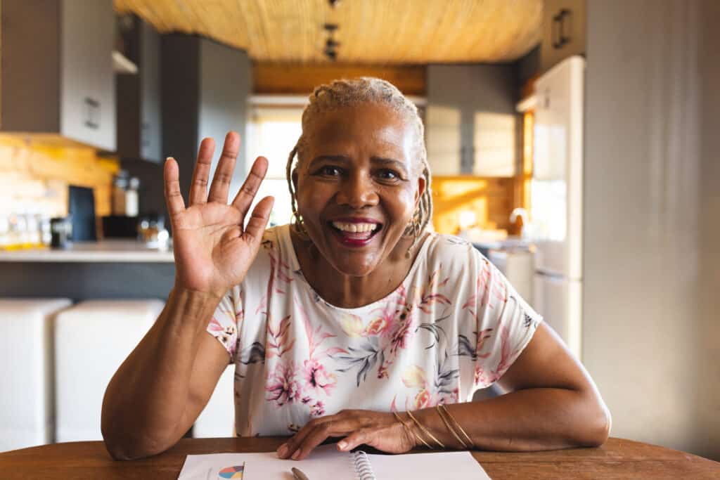 An older African American woman at the kitchen table waves hello