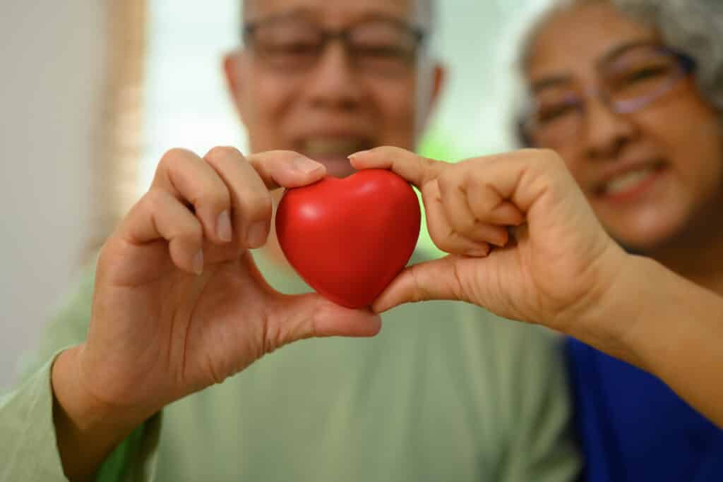 Happy senior couple holding a small heart; coronary artery disease is common among both men and women to varying degrees.