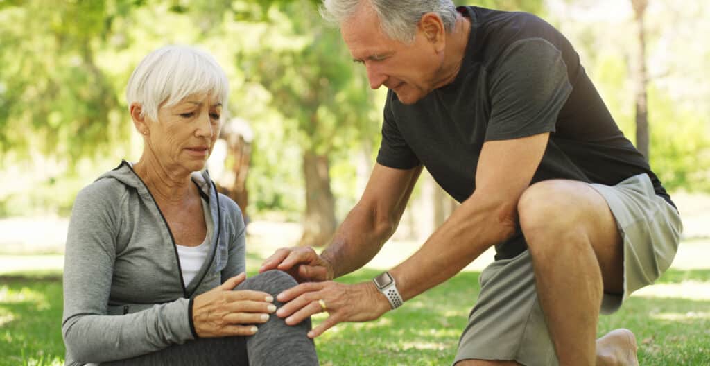 The difference between pain and soreness is often determined by the cause: a senior woman is aided by her husband after a fall outdoors