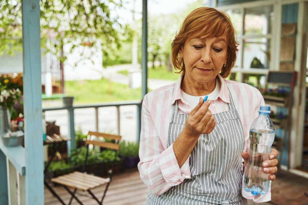 Plastics in the body: a senior woman uses a plastic water bottle to take her medication.