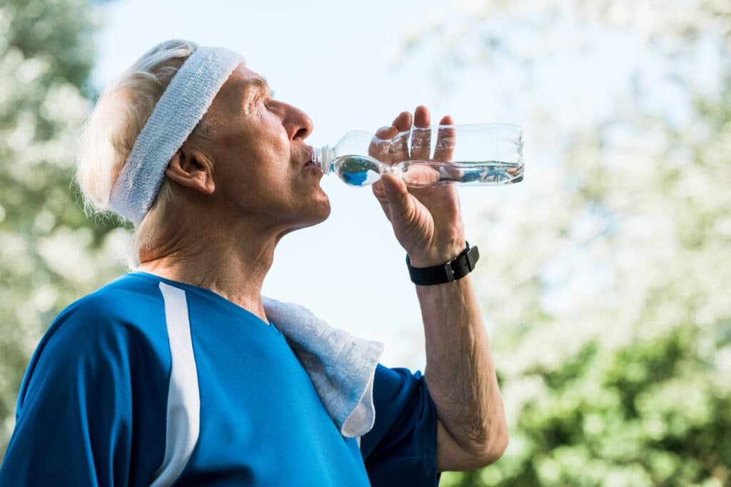 Dealing with the heat: an older man drinks water outdoors while exercising