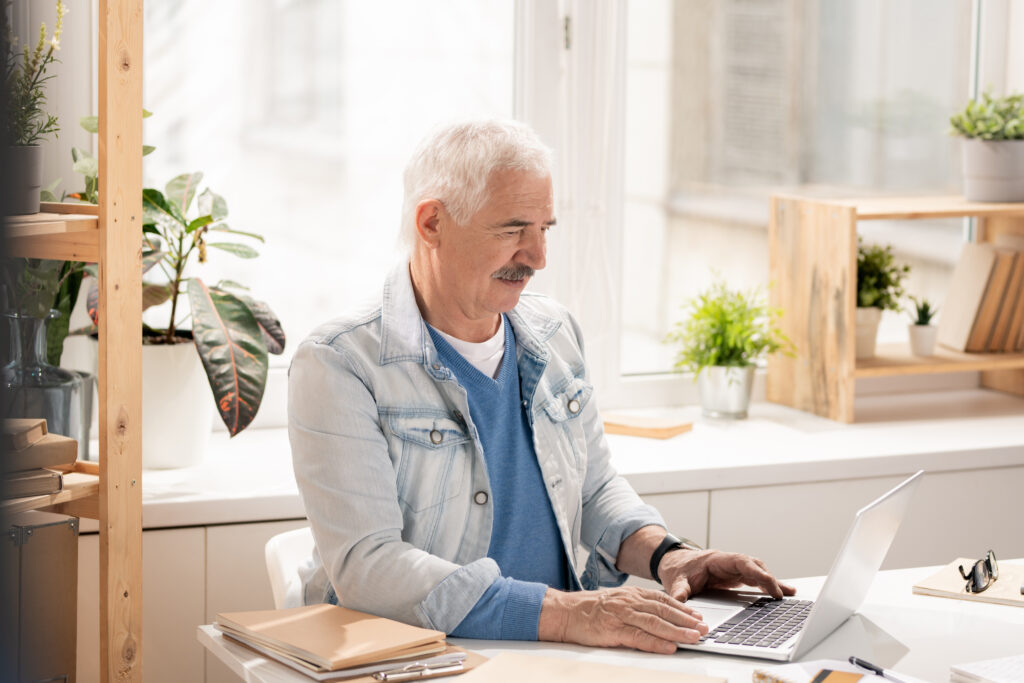 Casual senior office worker concentrating on analyzing online data while sitting by desk in front of laptop