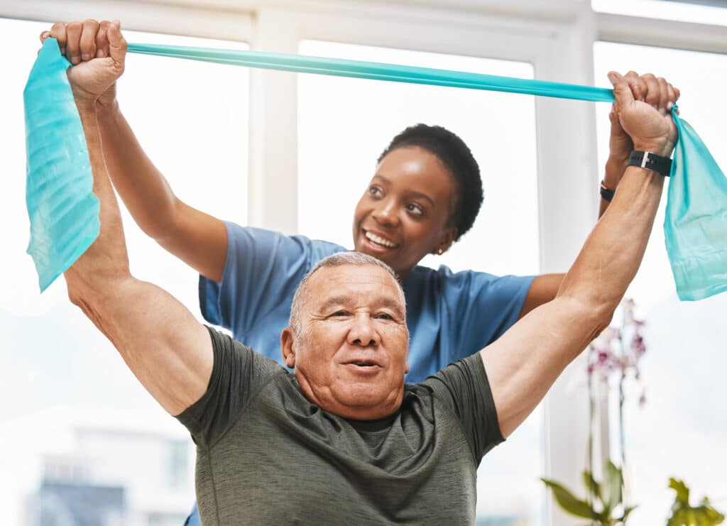 African American physical therapist helps an active older man with shoulder rehab exercises with a theraband.