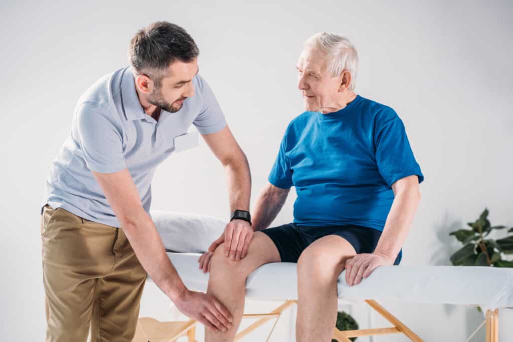 A physical therapist aids an older man with his knee pain