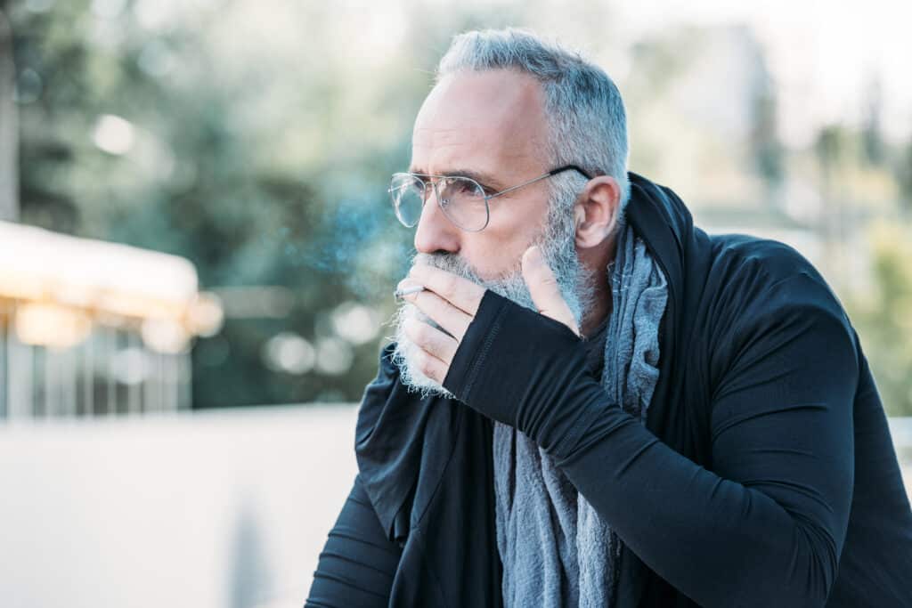 portrait of stylish senior man smoking cigarette on street; smoking is one of the most common factors leading to coronary artery disease