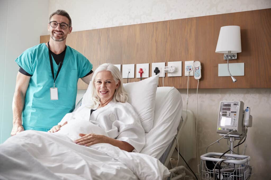 Improving Bone Health for Surgery: Image of a doctor visiting his happy senior patient in her hospital bed.