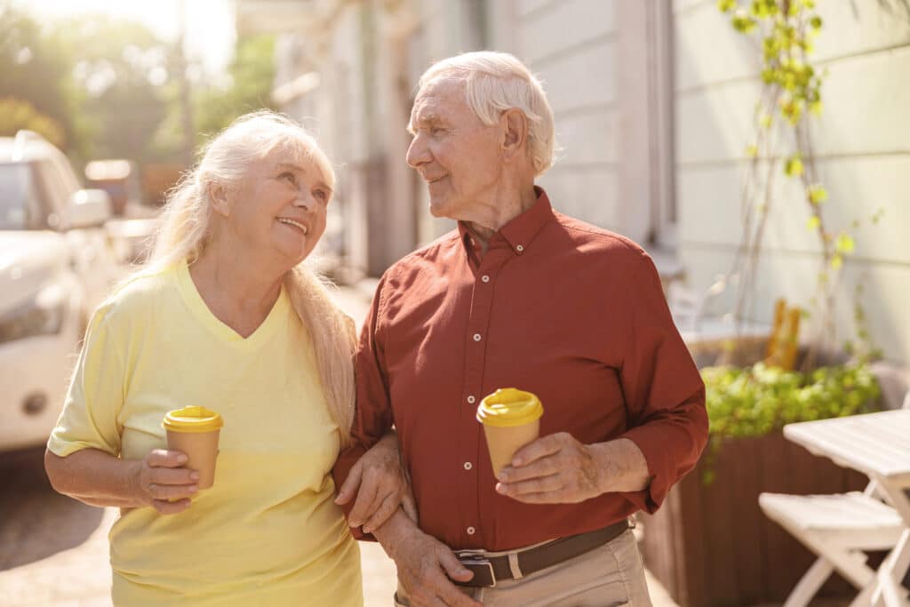 Image of senior couple walking outdoors and drinking coffee