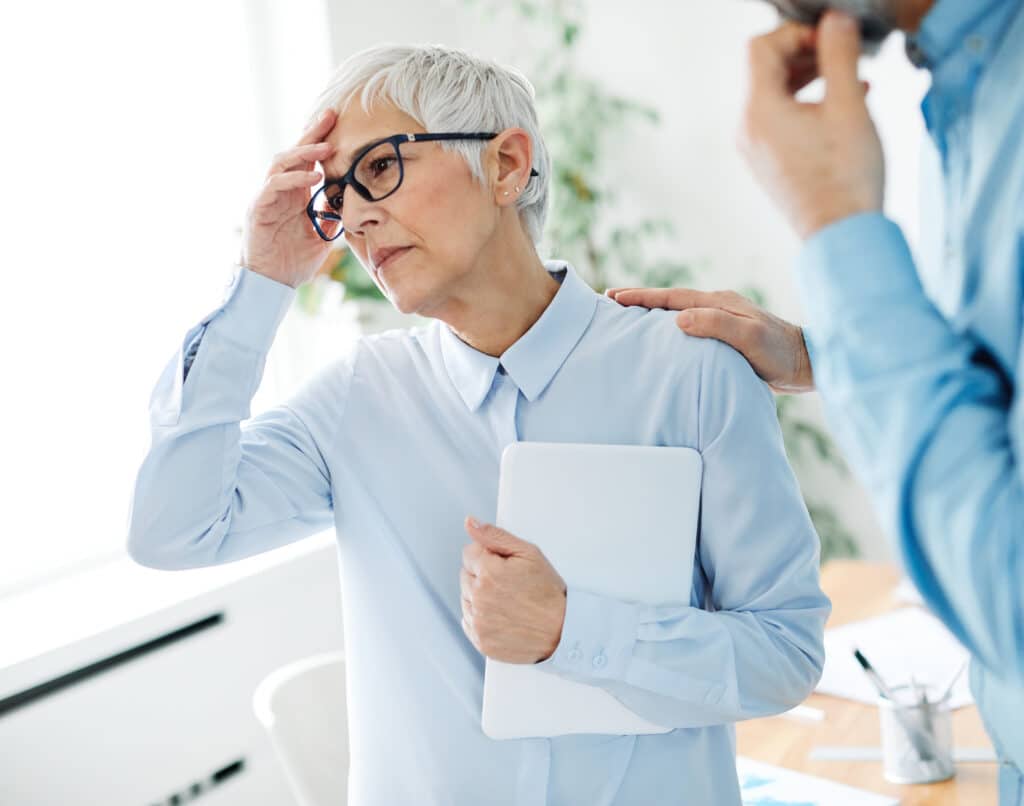 Stroke symptoms might include sudden headaches in the middle of your workday.  Image of a senior woman with a headache at work.