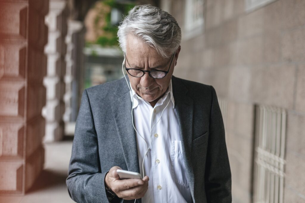 Senior businessman with earphones looking at cell phone