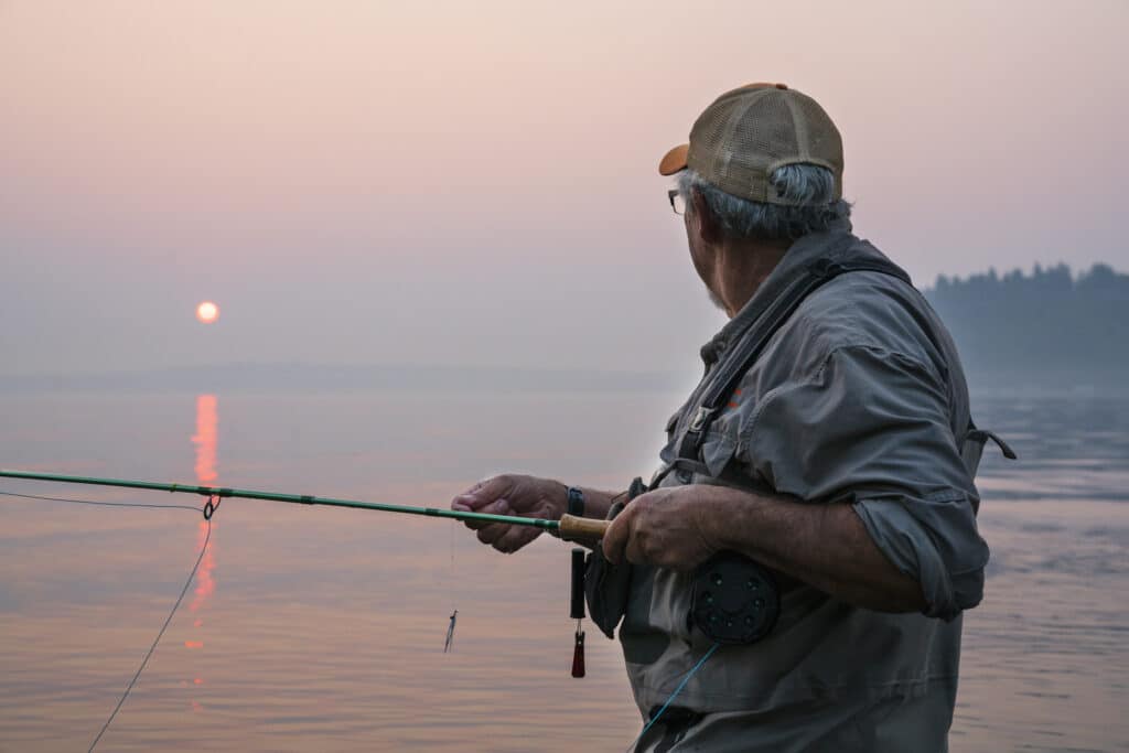 Senior man fishing on a hazy day after rotator cuff surgery.