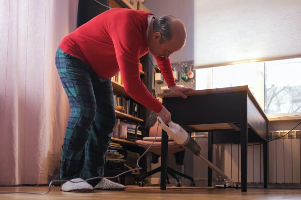 Senior caucasian man cleaning room fro dust with vacuum cleaner. Housework concept