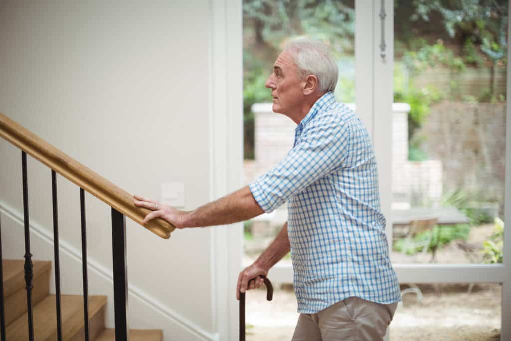 Knee pain when walking up stairs: image of a senior man preparing to ascend a flight of stairs with a cane.
