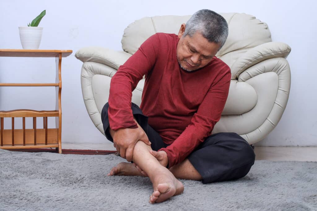 Senior Asian man rubbing his ankle due to peripheral neuropathy problems from diabetes.