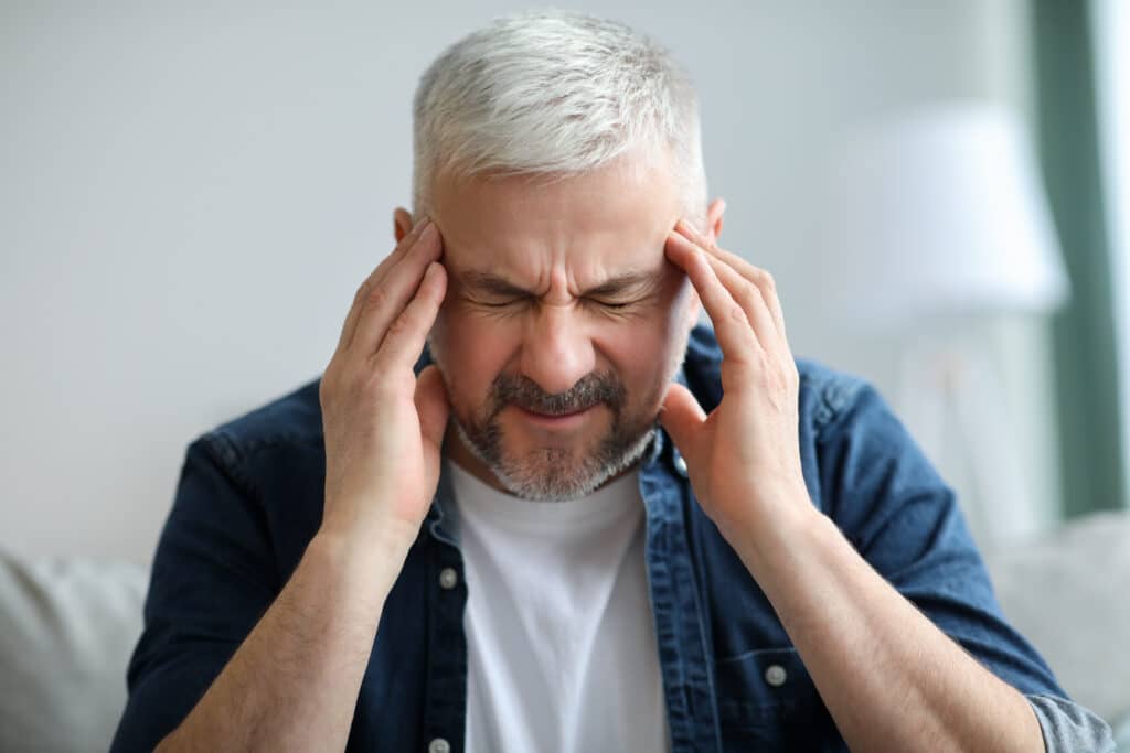 A gray-haired man holds his temples from a tension headache.