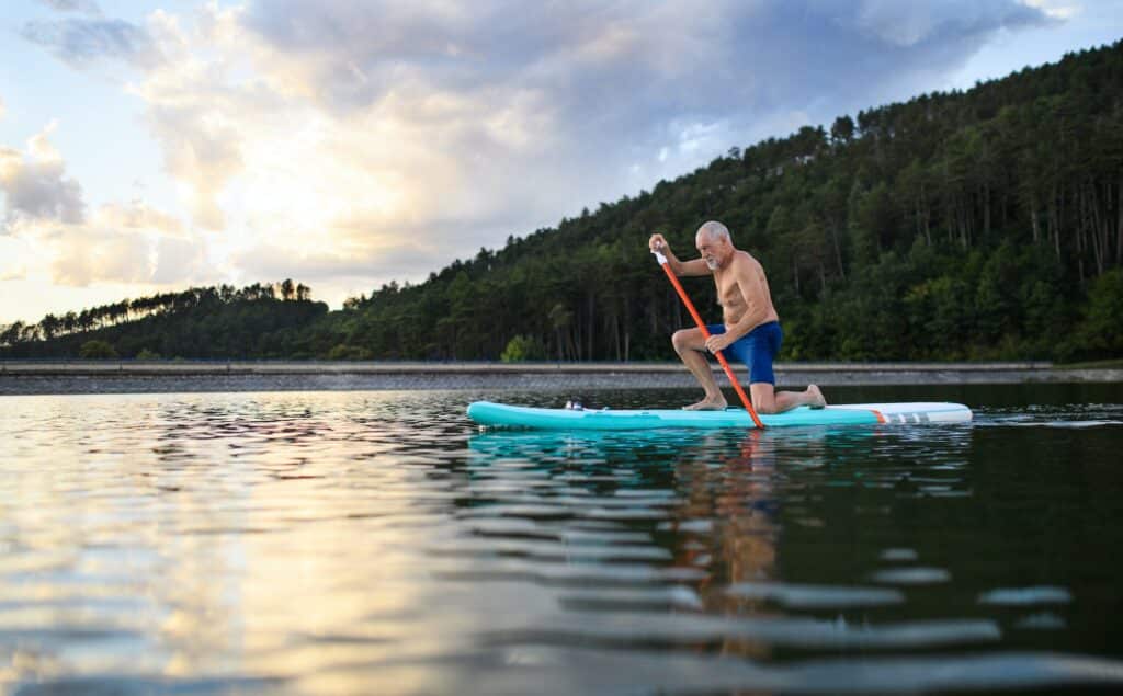 Senior man paddleboarding on lake in summer. Copy space