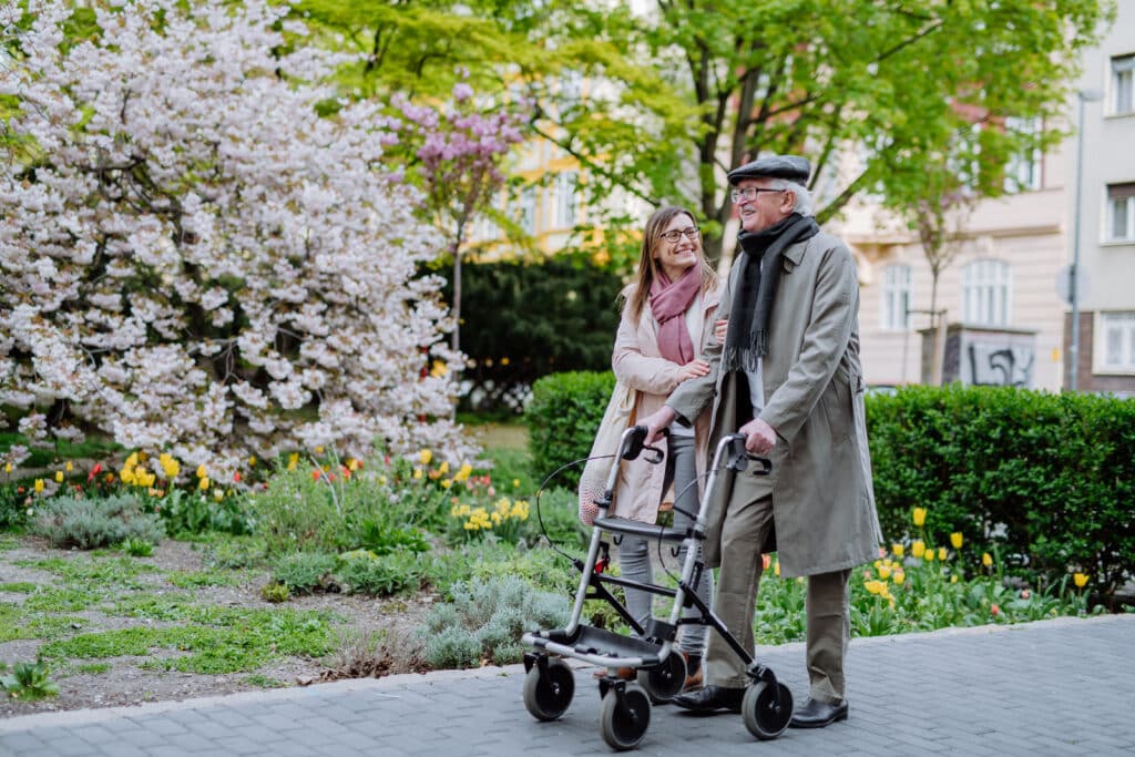 Rollator walker: a senior man walks with his walker and his wife in the park in springtime