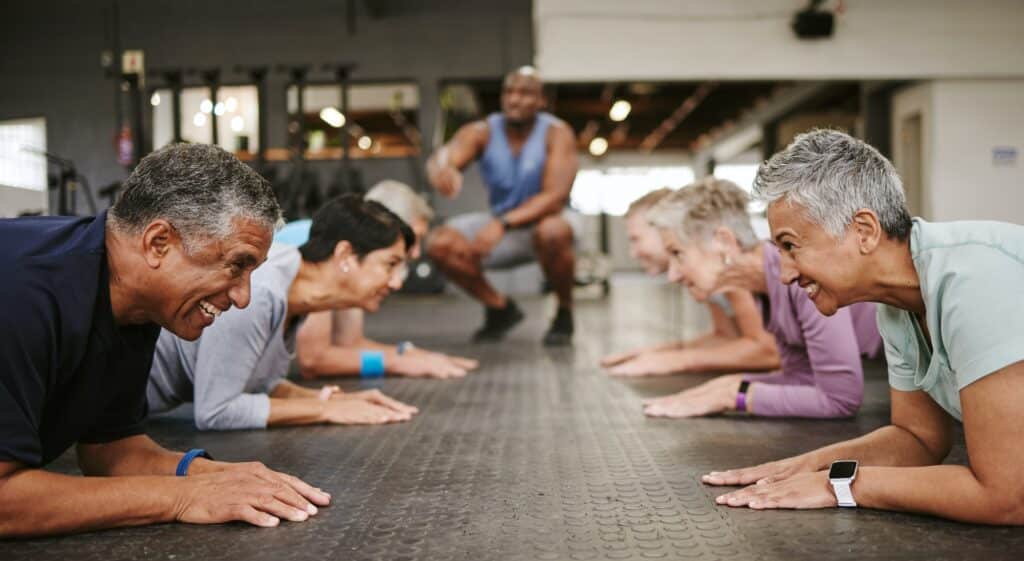 Senior people, fitness and plank with personal trainer in class for workout, core exercise or train