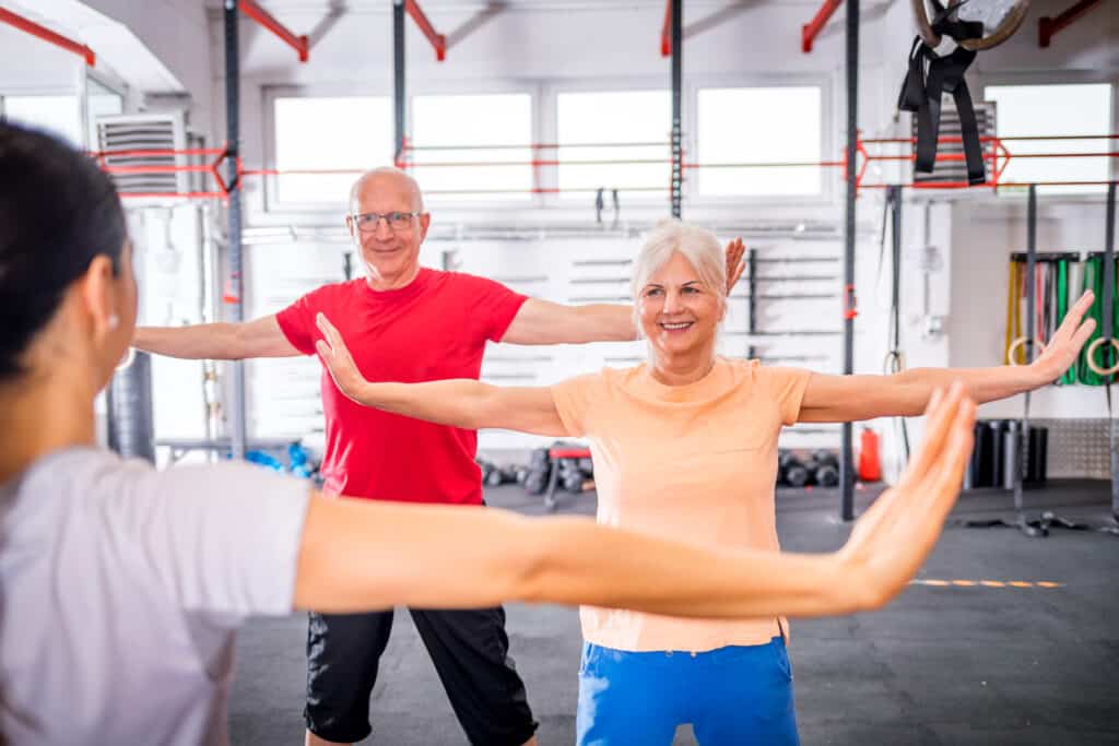 Image of senior couple doing shoulder exercises with a personal trainer in a gym