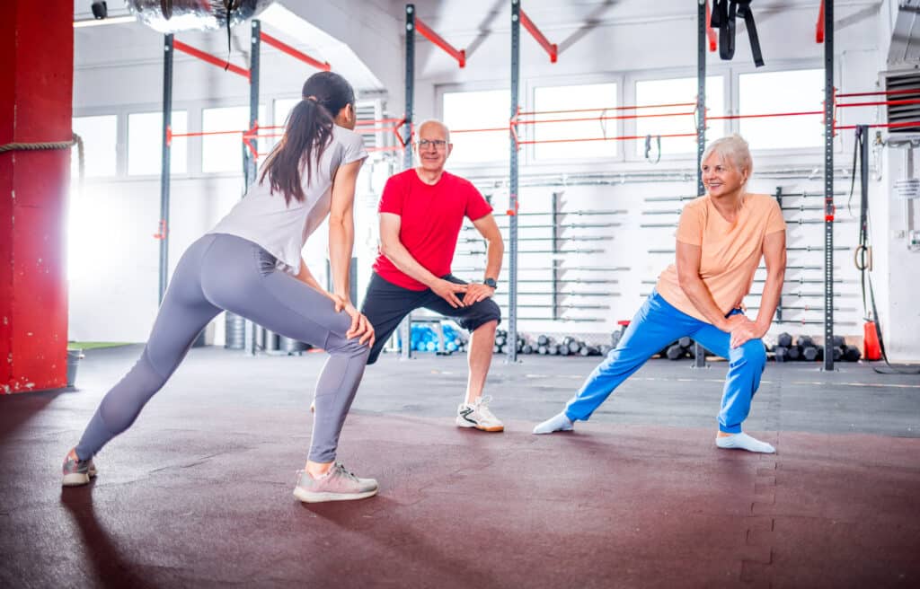 Knee bursitis exercises: a senior couple warms up with their personal trainer at the gym