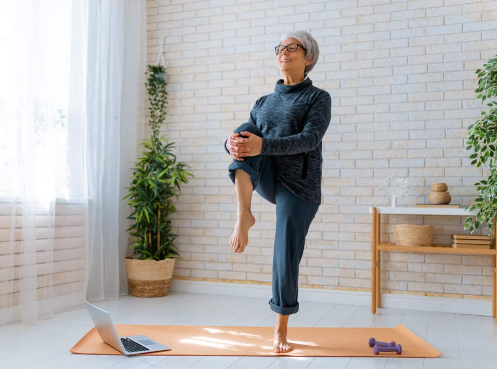 How to do a balance test at home: a senior woman does an online yoga class at home.