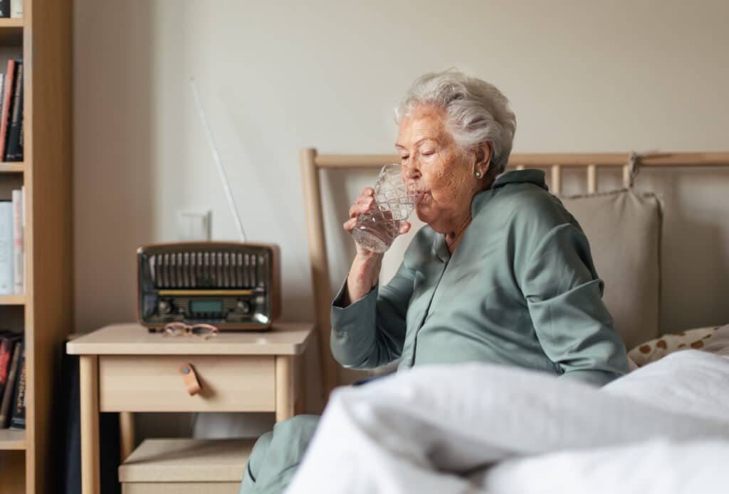 Image of a senior woman sitting up in bed drinking water