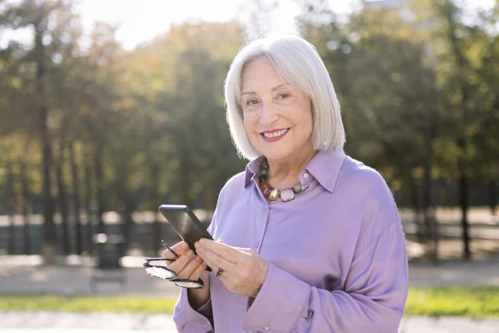 Many Parkinson's Disease Assistive Tools are available on smart phones—image of a woman holding her phone and smiling outdoors.