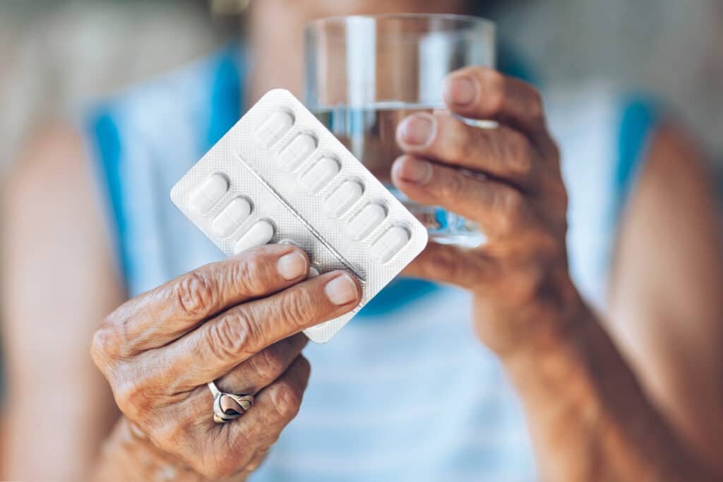 Image of an older African American woman holding prescription pills and a glass of water.