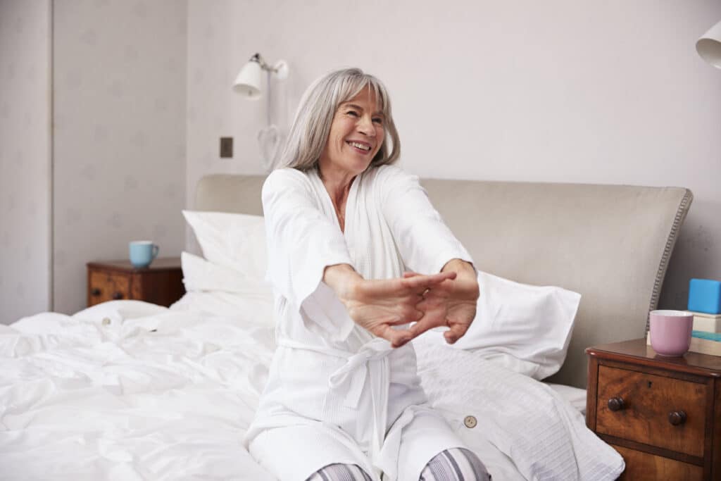 Senior woman stretching in bed after a good night's sleep.