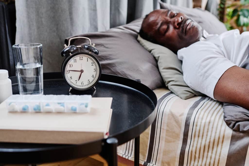 REM sleep disorder and Parkinson's: image of an African American man sleeping with medication on his nightstand