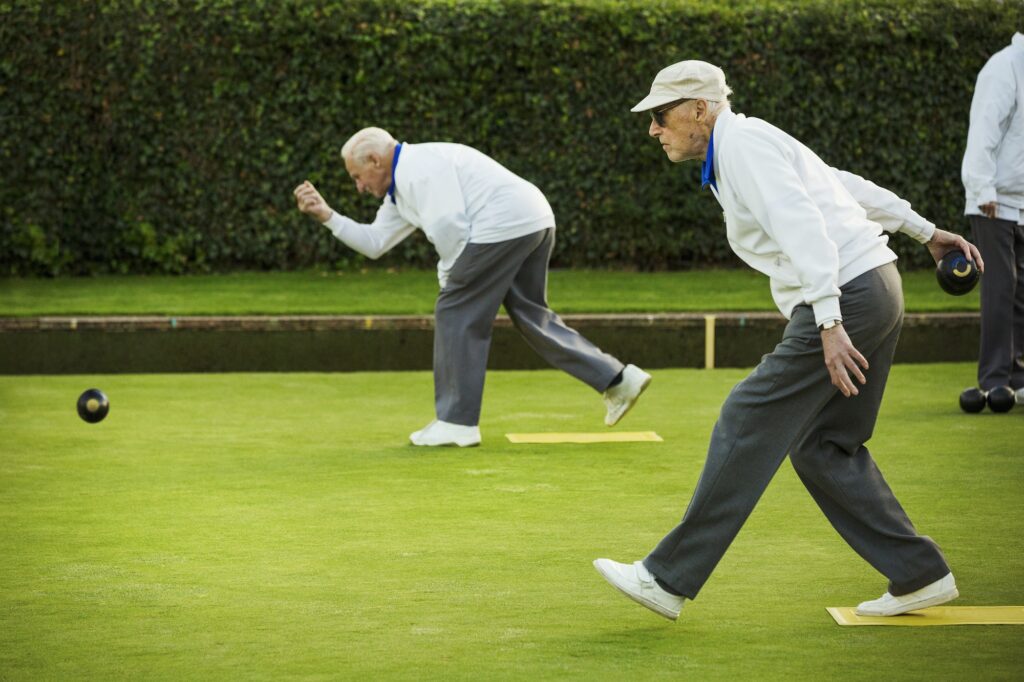 Two men preparing to deliver a lawn bowl shot, bending down and swinging their arms.