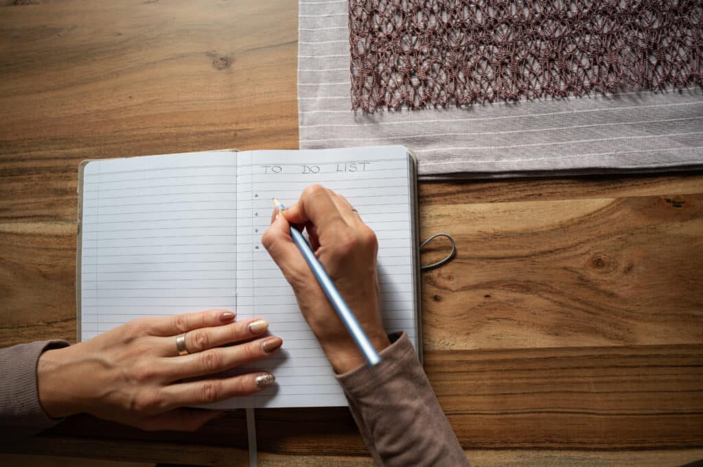 Image of a woman's hands writing a to-do list at a wooden desk.